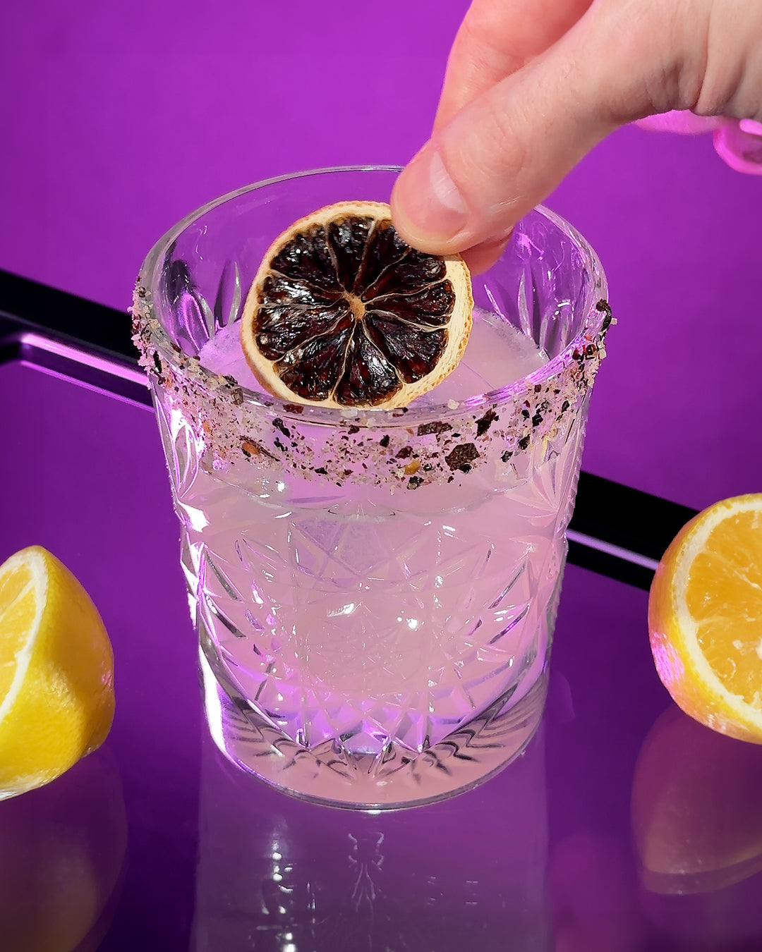 A hand placing a dried lemon wheel onto a Silencio mezcal margarita cocktail.