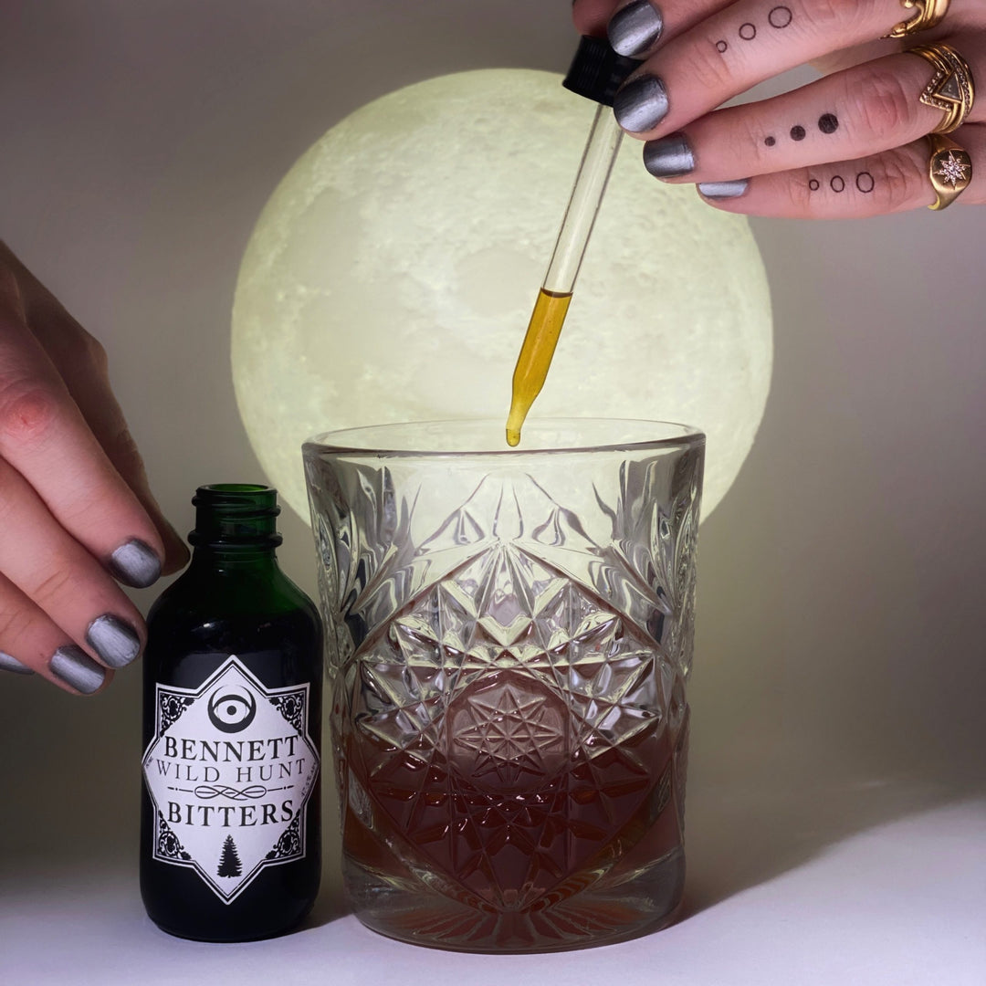 Hand dripping Herbal Wild Hunt Bitters by Bennett Bitters into a cocktail in a glass.