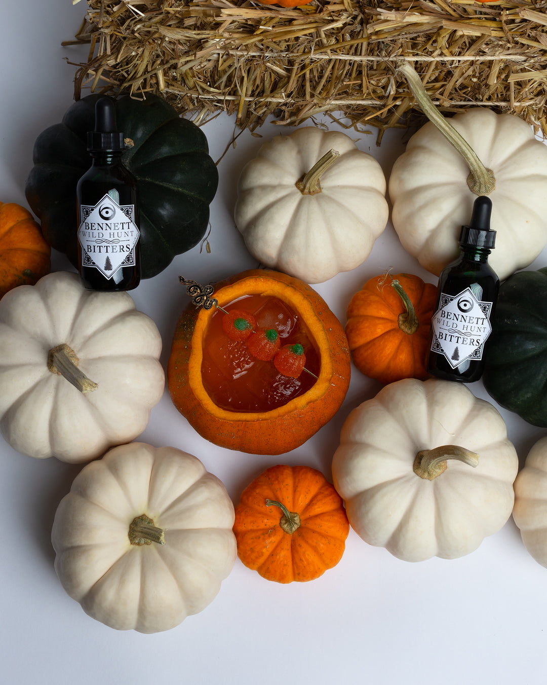 Tricky Treat peach whisky punch cocktail served in a carved out pumpkin, in a scene with many other pumpkins, and two bottles of Bennett Wild Hunt Bitters.