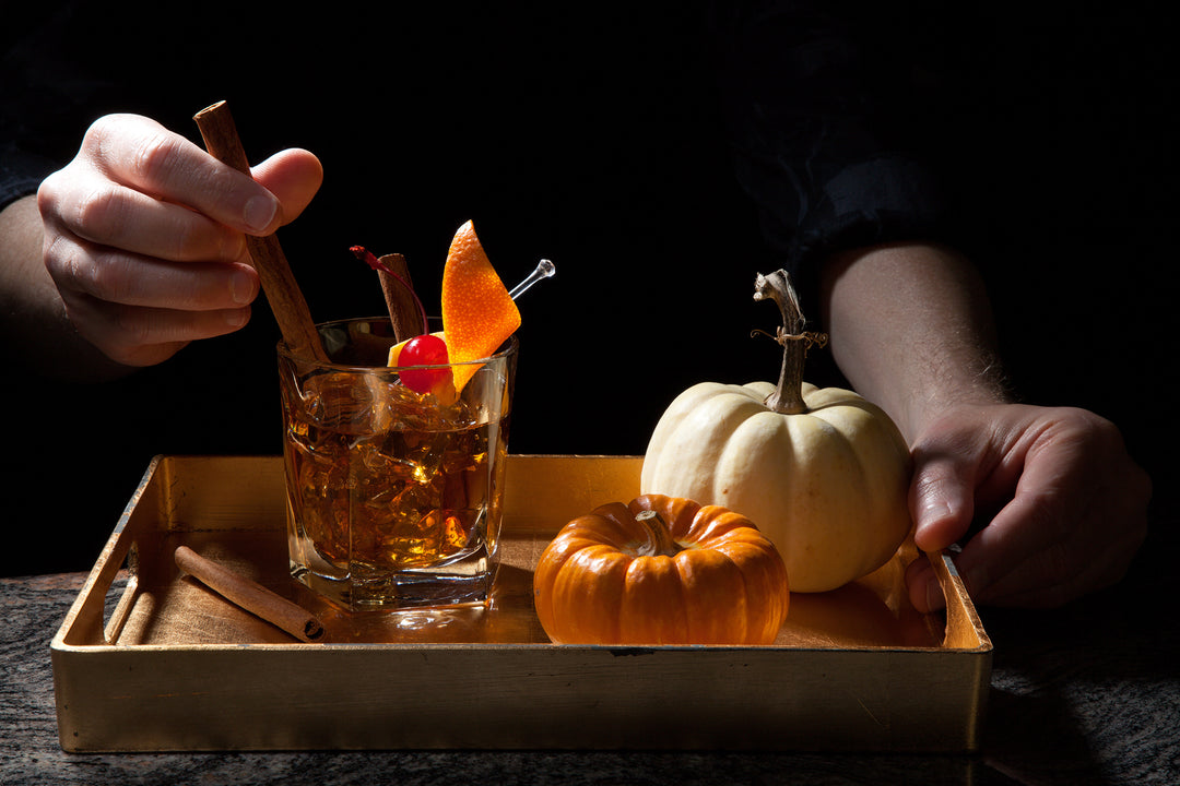 Hands making old fashioned cocktail, next to pumpkins.