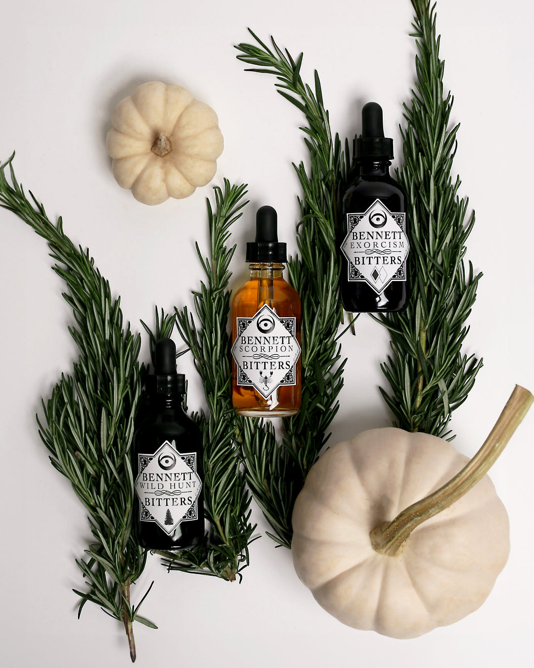 The Esoteric Collection by Bennett Bitters bottles laying down and surrounded by rosemary and white pumpkins.