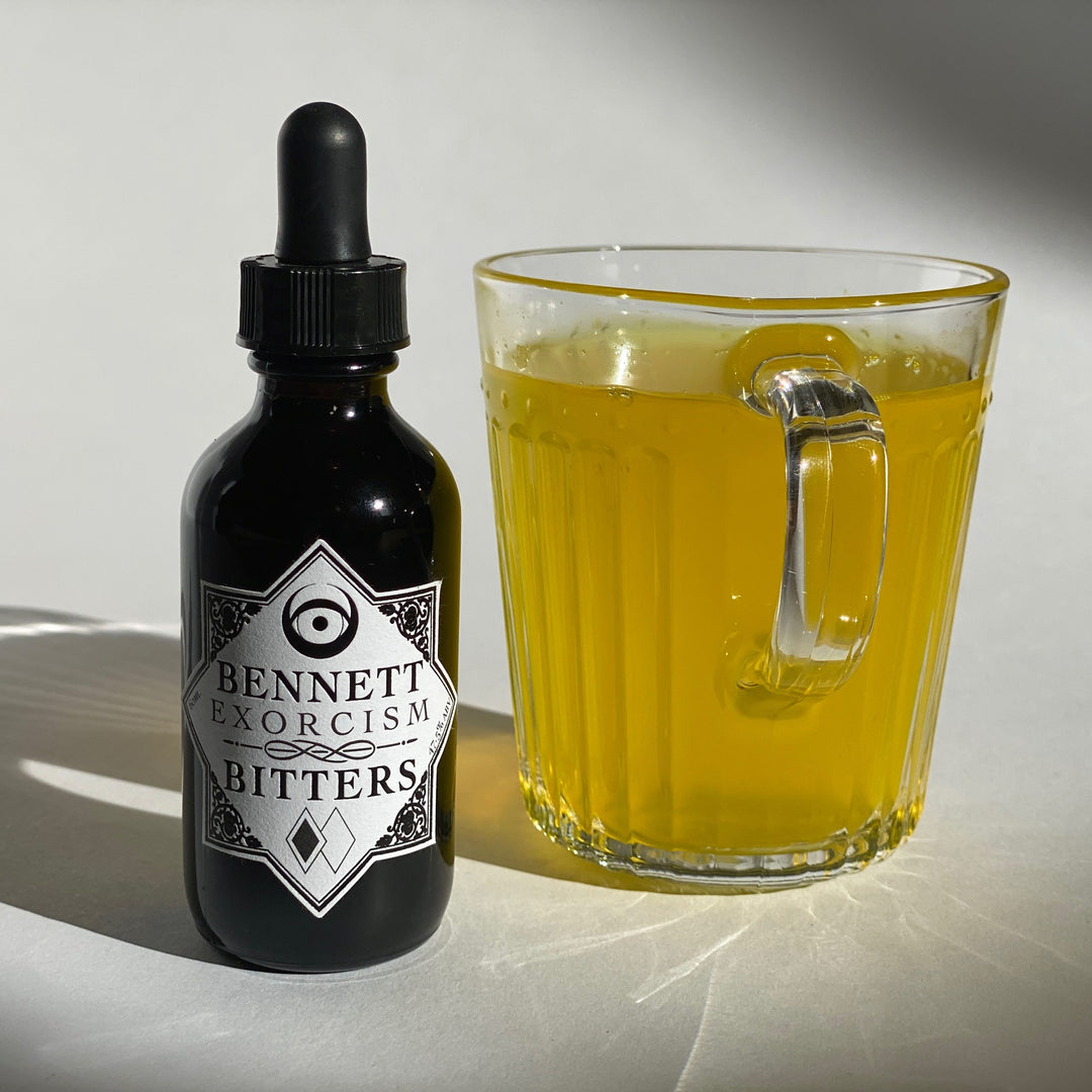 Aromatic Exorcism Bitters bottle by Bennett Bitters with bright yellow turmeric tea in a glass cup.