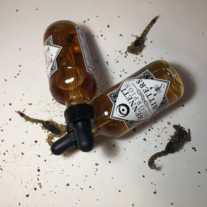 Two bottles of Spicy Scorpion Bitters by Bennett Bitters laying down surrounded by scorpions.